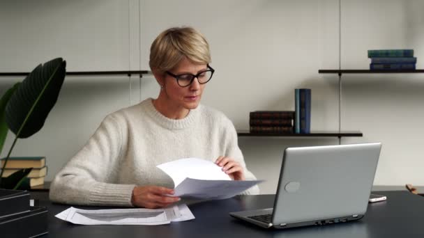 Retrato de uma mulher de negócios madura trabalhando em um laptop no local de trabalho no escritório, tira os óculos e pensa enquanto olha para o laptop — Vídeo de Stock