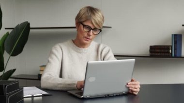 Masasında oturan orta yaşlı bir iş kadını gözlerindeki acıdan gözlüklerini çıkarır ve burnunun köprüsüne masaj yapar..