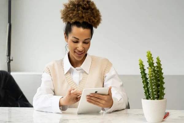 Retrato de una alegre y elegante mujer negra con ropa casual sentada en un escritorio usando una tableta en la oficina. — Foto de Stock