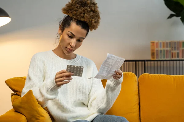 Hermosa mujer negra lee las instrucciones médicas para las pastillas. Una mujer sosteniendo un analgésico — Foto de Stock