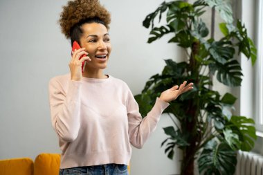Genç bir Afro-Amerikalı kadın oturma odasında telefonla konuşuyor. Ev ofisinde çalışan ve cep telefonu kullanan bir iş kadını..