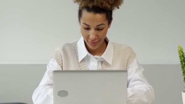 Young African-American female entrepreneur uses a laptop in the workplace and looks at the camera — Stockvideo
