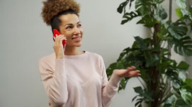 Genç bir Afro-Amerikalı kadın oturma odasında telefonla konuşuyor. Ev ofisinde çalışan ve cep telefonu kullanan bir iş kadını..