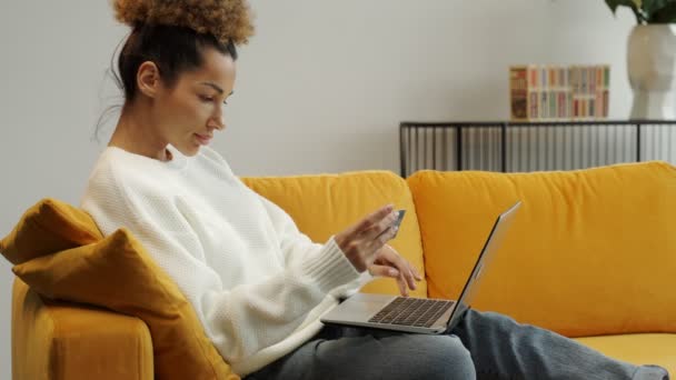 Jeune femme afro-américaine détenant une carte bancaire de crédit, entrant des informations de paiement dans une application d'achat en ligne, achetant des biens ou des services en ligne — Video