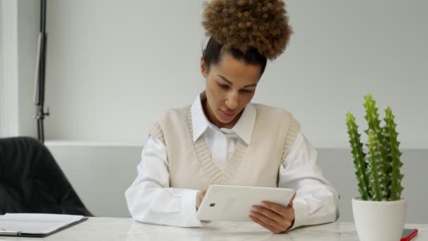 Czarna kobieta z kartą kredytową dokonuje płatności online za pomocą tabletu. Młoda, kręcone włosy kobieta siedzi za biurkiem — Wideo stockowe
