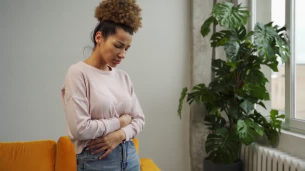 Nespokojená Afroameričanka s kudrnatými vlasy trpí bolestí břicha, oběma rukama se dotýká břicha, dívá se na menstruaci — Stock video