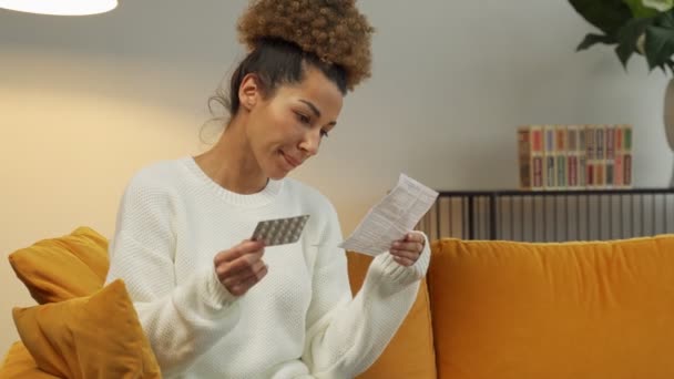Hermosa mujer negra lee las instrucciones médicas para las pastillas. Una mujer sosteniendo un analgésico — Vídeos de Stock