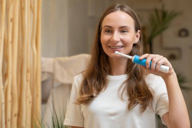 Parlak bir banyoda dişlerini mor bir diş fırçasıyla yıkayan güzel bir genç kadının ayna görüntüsü. Günlük ağız temizliği kavramı