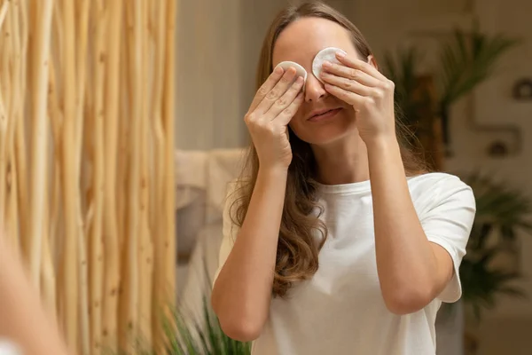 Mujer joven usando almohadilla de algodón mientras limpia su cara en el baño — Foto de Stock