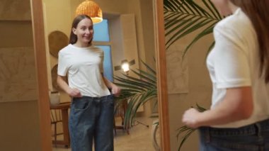 Diyet yüzünden çok kilo veren bir kadın aynaya bakar ve büyük kot pantolon gösterir.