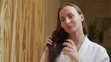 Çekici, bornozlu neşeli esmer evde duş aldıktan sonra banyoya saç kremi sürüyor. Saç bakımı