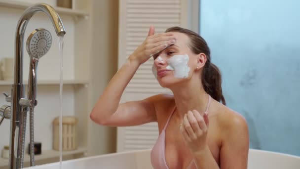 Giovane ragazza applica uno scrub viso per la pelle mentre seduto in bagno — Video Stock