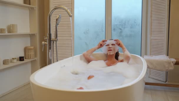 Jonge vrouw met een masker op haar gezicht ligt in de badkamer. — Stockvideo