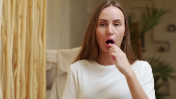 Tükörkép egy gyönyörű fiatal nőről, aki fogat mos egy lila fogkefével egy fényes fürdőszobában. A napi szájhigiénia fogalma — Stock videók