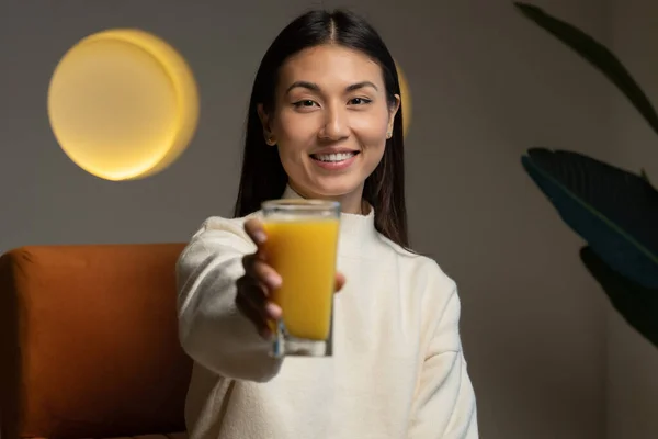 Beautiful Asian woman holds a glass of orange juice in her hand and looks at the camera — стоковое фото