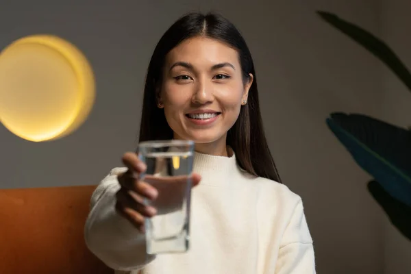 A happy beautiful young Asian woman holding a clear glass of clean water in her hand and looking at the camera. Portrait of a happy smiling young woman with a glass of fresh water — стоковое фото