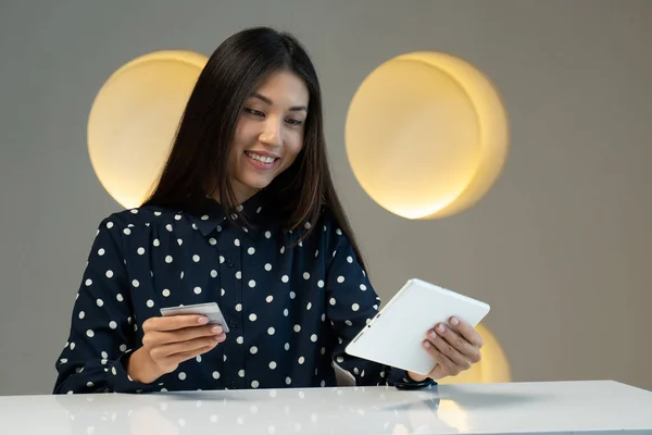 Una mujer asiática usando una tarjeta bancaria para pagar los bienes comprados en línea usando una tableta en una mesa — Foto de Stock
