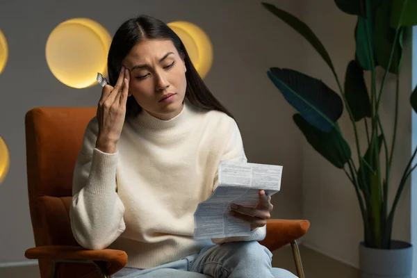 Una mujer asiática toma medicamentos para el dolor de cabeza. Una joven sostiene un paquete de pastillas en su mano y lee instrucciones médicas.. — Foto de Stock