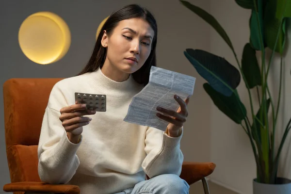 Asian woman takes medicine. A young woman holds a package of pills in her hand and reads medical instructions. — Stockfoto