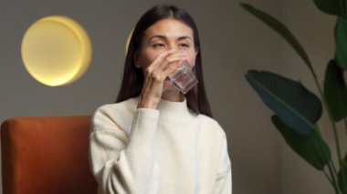 Young asian woman drinking water. Smiling female model holding transparent glass in her hand. 