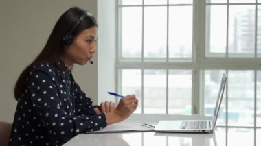 Asian young student use wireless earbuds to have online courses and searching information via laptop computer
