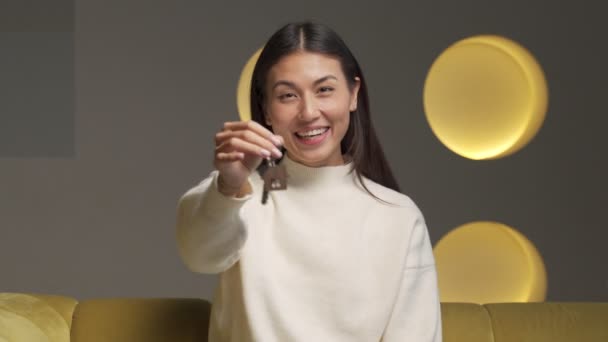 Potret seorang penyewa wanita Asia yang tersenyum menunjukkan kunci apartemen baru, melihat ke kamera, seorang pelanggan yang gembira ingin membeli rumah baru — Stok Video