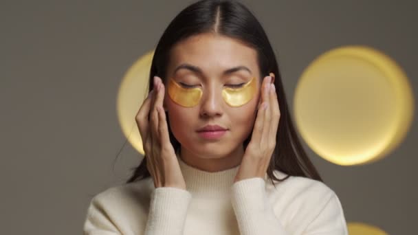 Young Asian woman with clear radiant skin with moisturizing golden patches under her eyes — Stockvideo