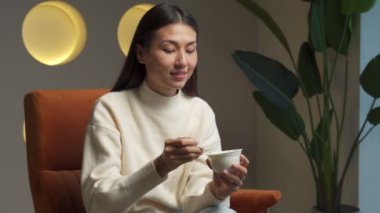 Cute young woman eating yogurt sitting at home on a chair
