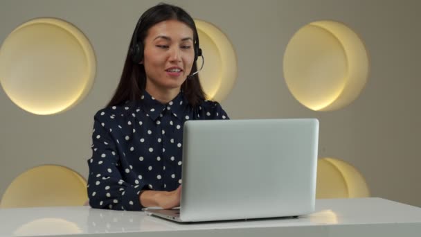 Smiling Asian woman in a headset, working in the office as a customer support service, sitting in the office — Αρχείο Βίντεο