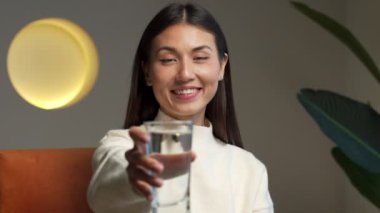 A happy beautiful young Asian woman holding a clear glass of clean water in her hand and looking at the camera. Portrait of a happy smiling young woman with a glass of fresh water