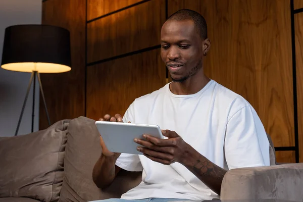 Joven hombre negro usando su tableta digital en casa sentado en el sofá — Foto de Stock