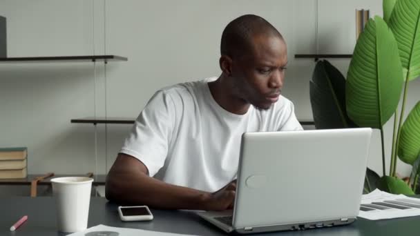 Профессиональный черный человек ищет необходимую информацию на ноутбуке, звонит по телефону, пьет кофе — стоковое видео