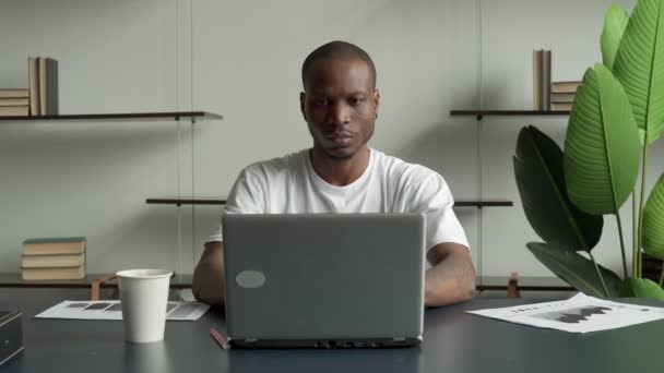 Porträt eines lächelnden schwarzen Mannes, der einen Laptop benutzt und in die Kamera schaut, während er die Arbeit in einem Bürointerieur genießt — Stockvideo