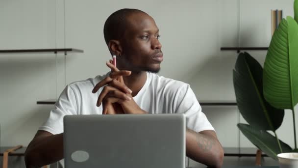 Düşünceli siyah iş adamı bilgisayarla bir masada oturuyor ve başka tarafa bakıyor. Dersleri yüzünden dikkati dağılan genç adam düşünceye daldı. — Stok video