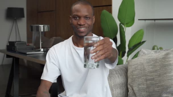 Ein hübscher junger schwarzer Mann hält ein Glas frisches, kühles Wasser in den Händen — Stockvideo
