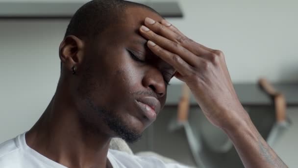 Черный мужчина испытывает сильную головную боль, от которой страдает, прикасаясь к голове, с закрытыми глазами из-за боли — стоковое видео