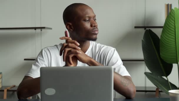 Homem de negócios preto pensativo sentado em uma mesa com um computador e olhando para longe. Distraído de seus estudos, o jovem mergulhou no pensamento — Vídeo de Stock