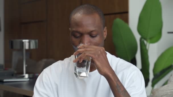 Jovem negro sentado no sofá bebendo água limpa de um copo — Vídeo de Stock