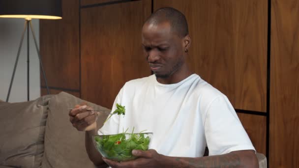 Joven hombre negro forzándose a comer ensalada, insatisfacción, dieta para el control de peso — Vídeo de stock