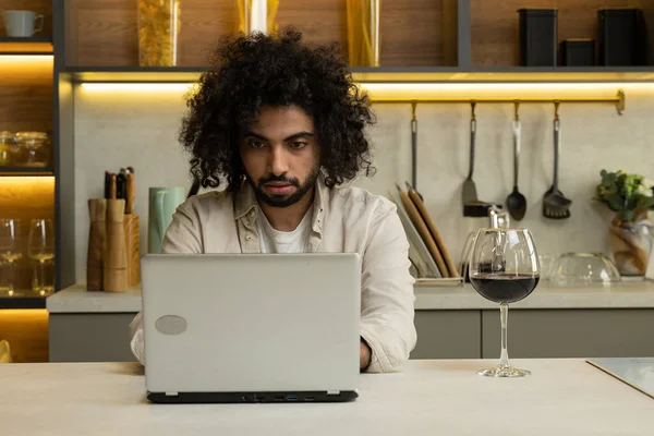Hombre árabe trabaja en línea en el ordenador portátil disfrutando de una copa de vino — Foto de Stock