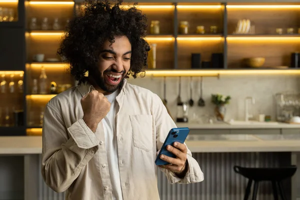 Мусульманин играет в игру и выигрывает в смартфоне на кухне — стоковое фото