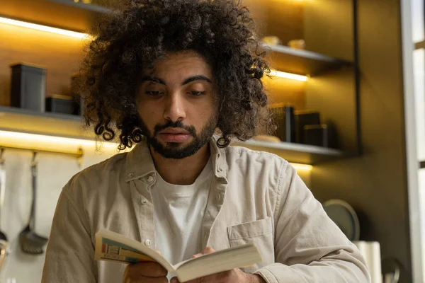 Muslim man reads book with recipes in kitchen at home