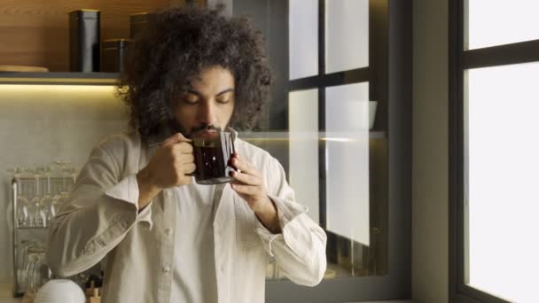Hombre musulmán disfruta del té caliente de pie cerca de la ventana en la cocina — Vídeo de stock