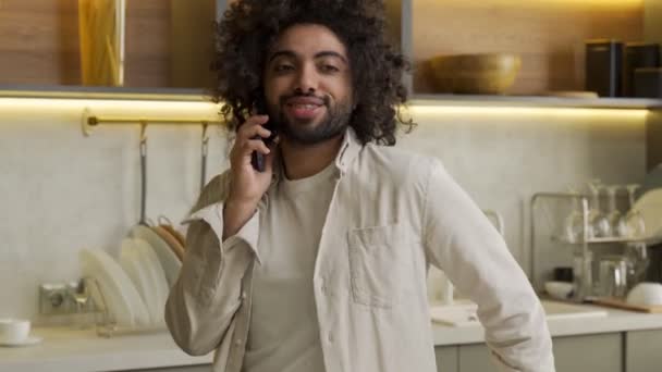 Vrolijke Arabische man praat over de telefoon met een vriend in de keuken — Stockvideo