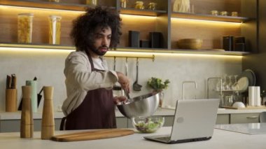 Mısırlı adam masadaki dizüstü bilgisayarda salata pişiriyor.