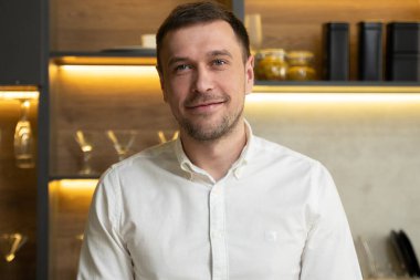 Genç adam kameraya bakıyor ve gülümsüyor.