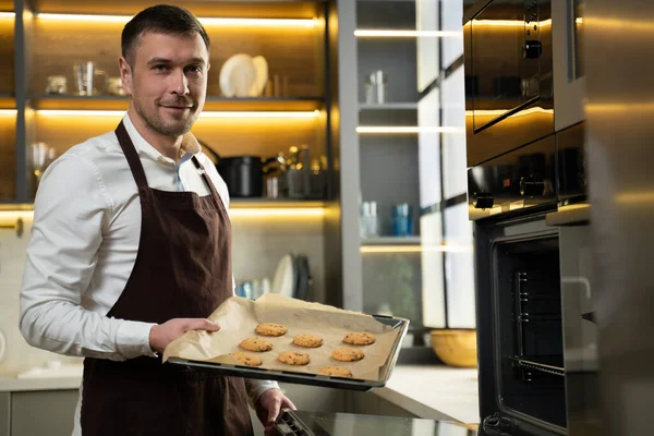 Joven chef toma galletas horneadas del horno en la cocina Imagen De Stock