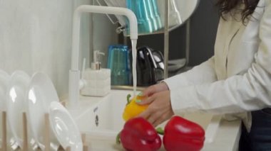 Genç kadın mutfakta akan suyun altında biber yıkıyor.