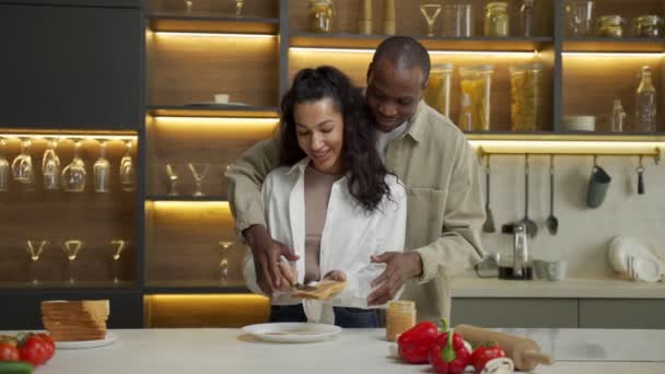 El hombre ayuda a la mujer amada difundir salsa en el pan en la cocina — Vídeos de Stock