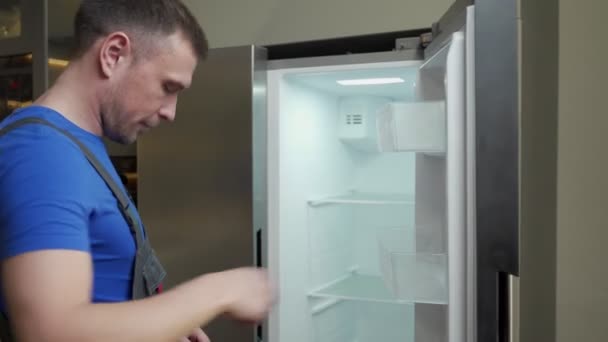 Foreman en uniforme intenta arreglar la nevera rota en la cocina — Vídeo de stock